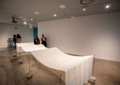 An installation view of a long piece of thin fabric suspended with a series of rectangular wire frames.